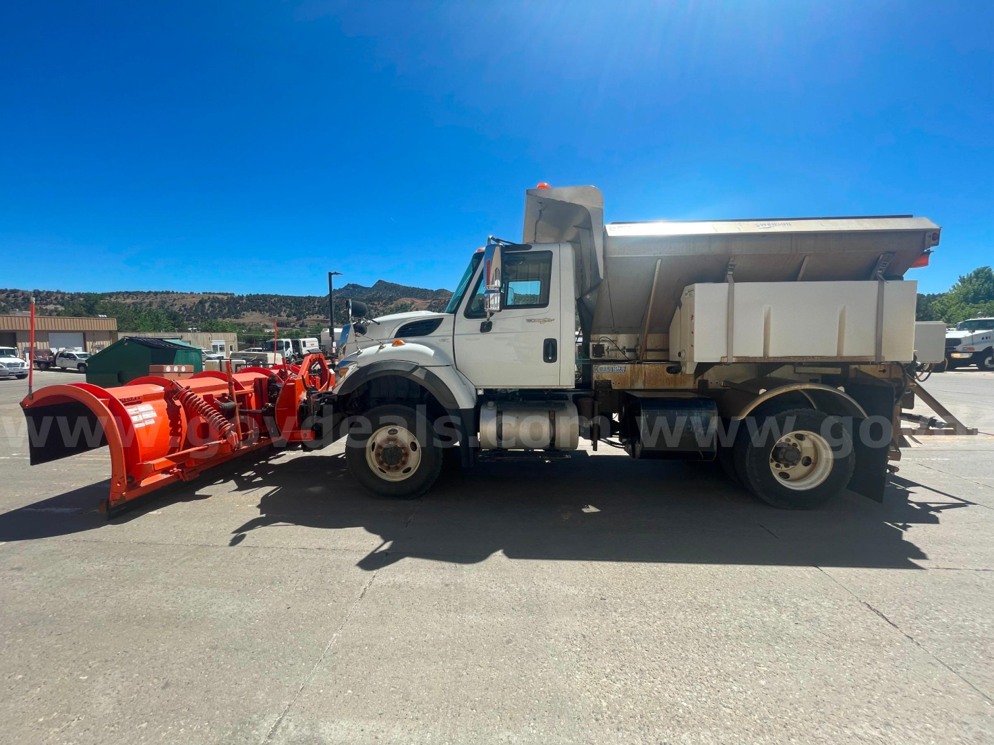 International truck dump bed with front cab and snow plow attachment in foreground.