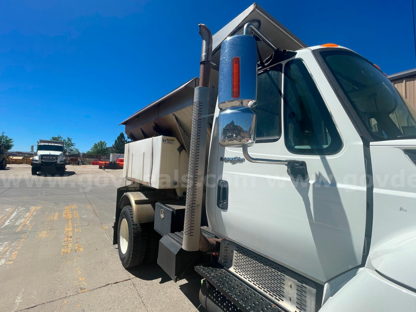 Truck cab with side mirror, dumping bed, blue vertical exhaust, chrome steps; visible text on side windshield area says 'International' logo and general truck components.