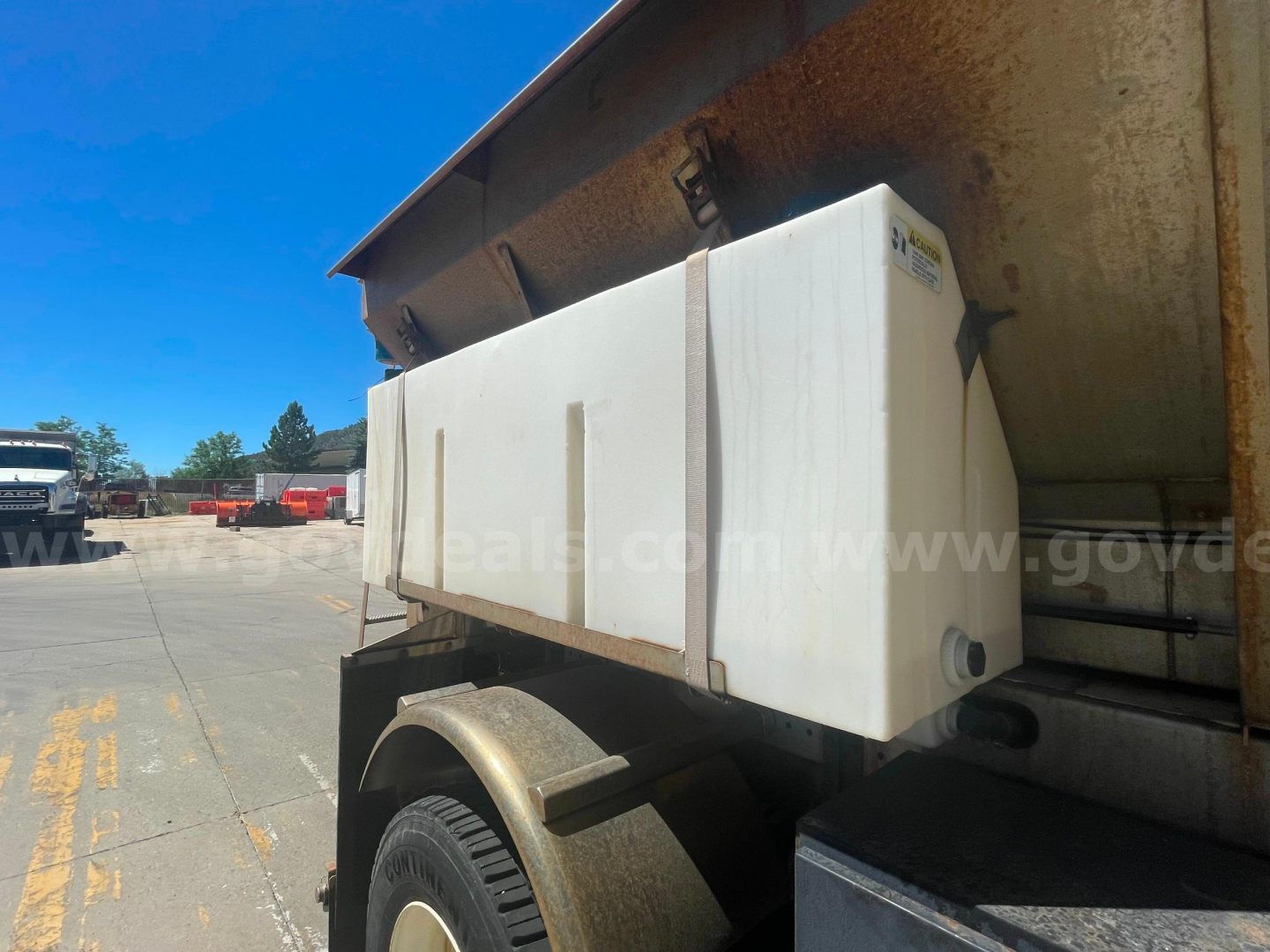 Truck bed with white plastic fuel/water tank mounted on utility truck, side view