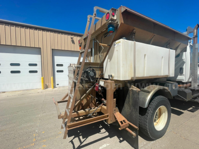 Dump truck bed system showing mounting frame and hydraulic tank on International 7400, rear view with ladder and wheel.