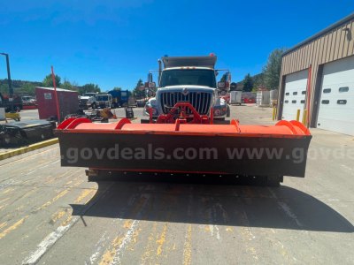 Front view of a 2012 International 7400 dump truck with a red snow plow attachment, visible grille and cab in background.