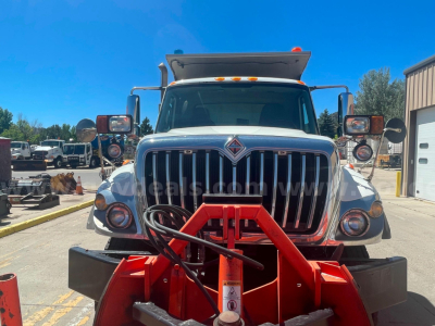 Truck front view showing International 7400 with red snowplow blade attached and chrome grille.