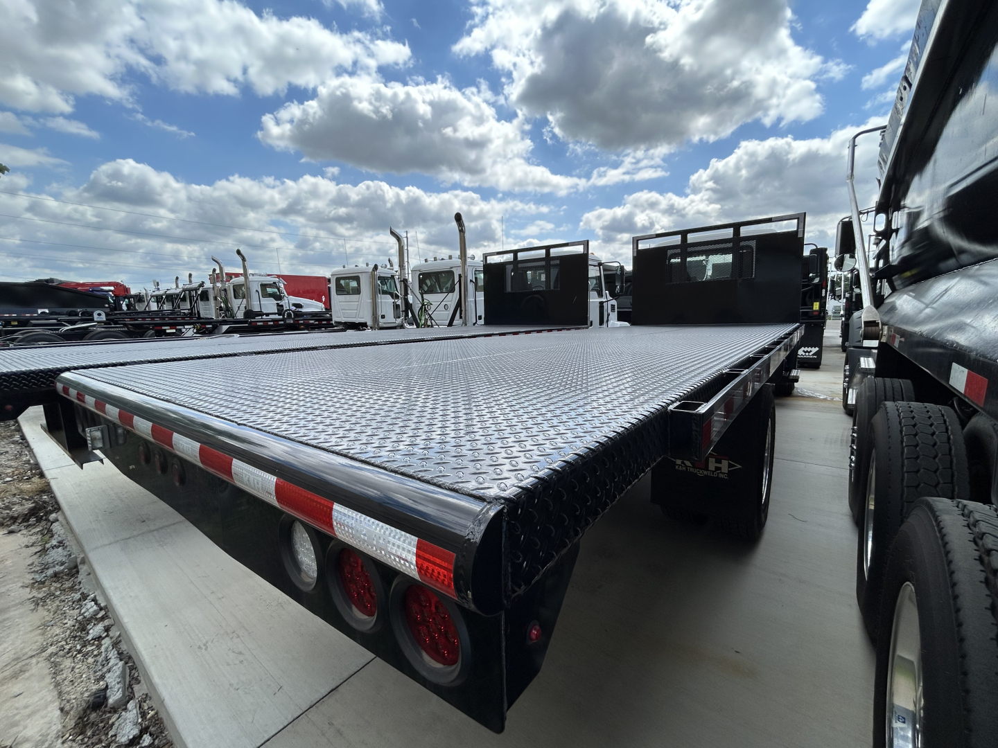 Flatbed truck bed of a 2026 Mack MD6 with diamond plate steel deck and rear triple taillights visible.