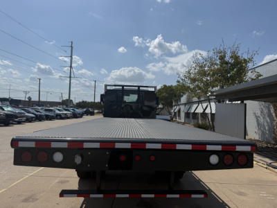 Flatbed truck bed of a 2026 Mack MD6 showing rear with taillights, reflective stripes, and a heavy-duty flatbed surface.