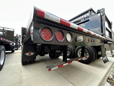 Truck flatbed rear showing KWH lighting, red/white reflective tape, multiple round taillights, mud flaps, and undercarriage with side rails.