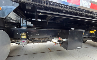 Mack MD6 truck undercarriage showing fuel filter, lines, and flatbed frame with toolbox and wiring harness.