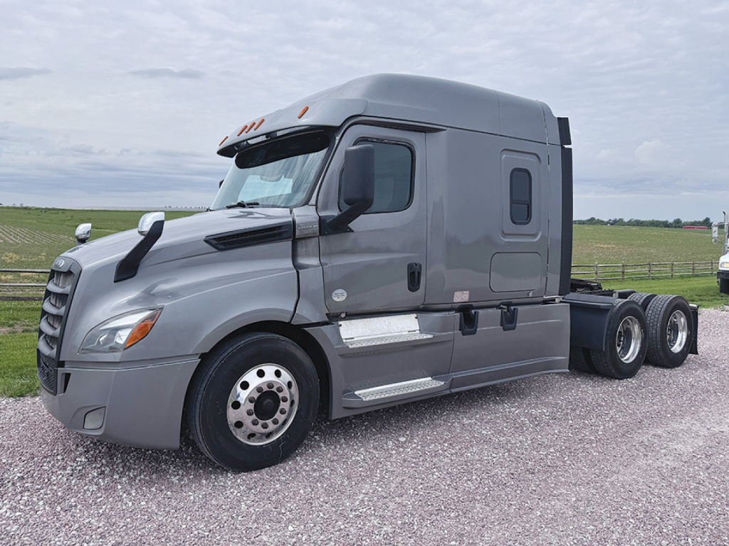 Freightliner Cascadia126 sleeper cab tractor in a light gray color, side view showing front wheel, door, side mirrors, cab doors, and three rear axles. No visible text readable on the image.