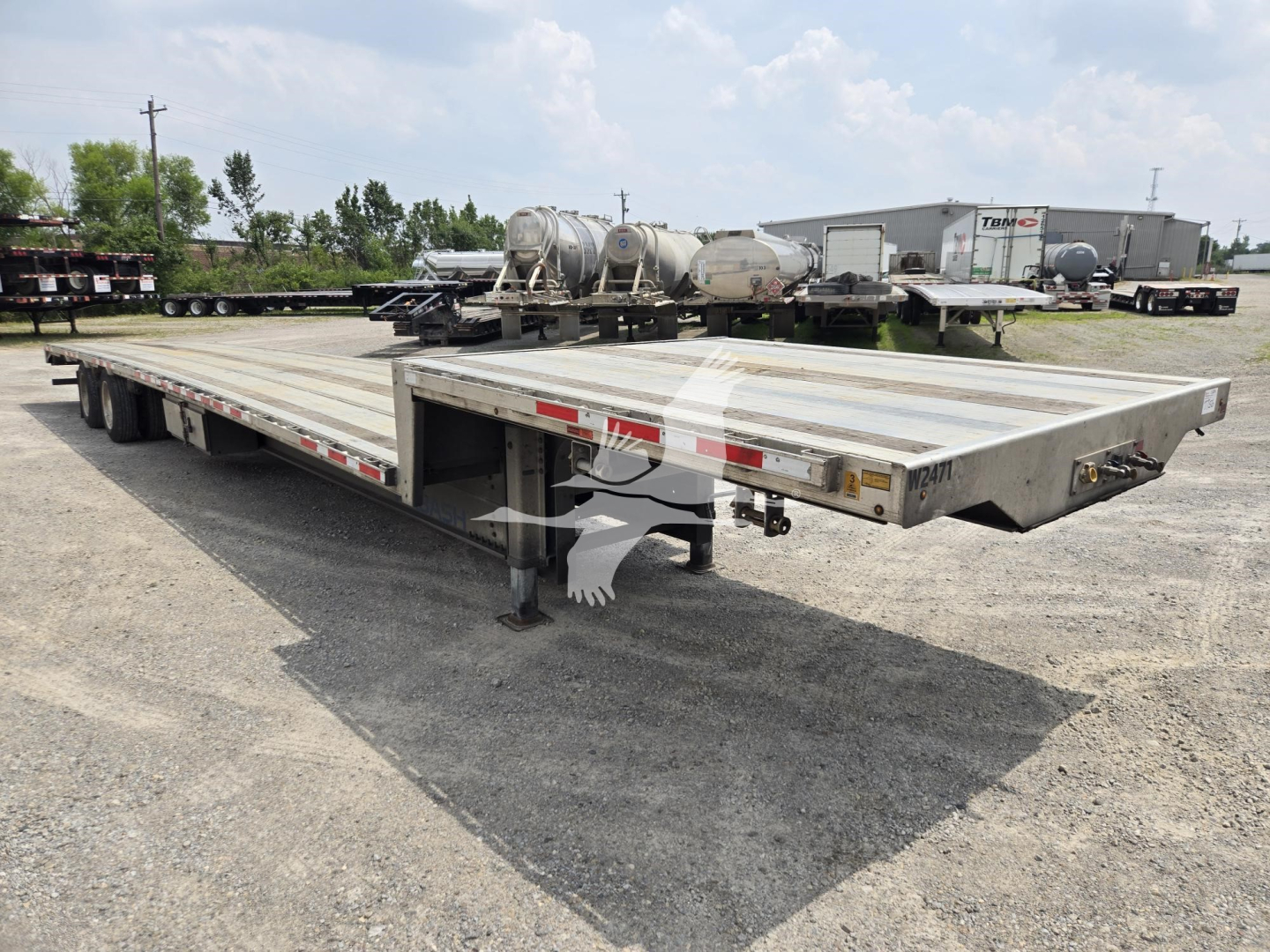 Trailer deck showing a Wabash drop deck trailer with metal flat bed, twin axles in background, and front hitch area visible.