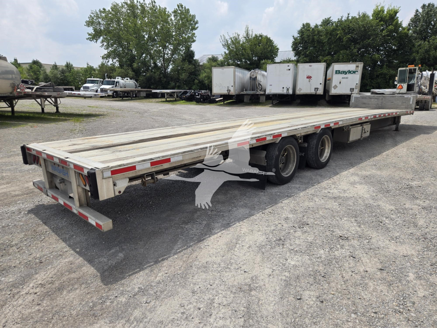 Trailer in a lot showing a long aluminum drop deck with dual rear axles and reflective tape