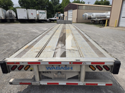 Wabash flatbed trailer rear view showing long metal deck with center rails, WABASH branding, red/white reflectors, and stock number plate at rear.