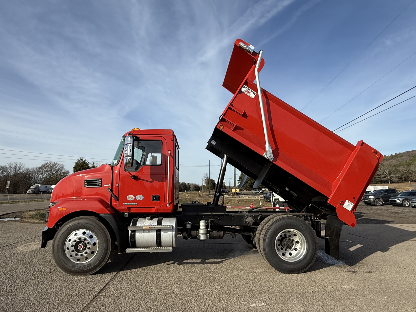 2025 Mack MD7 dump truck side profile showing dump bed raised, red cab, chrome exhaust, dual rear wheels, VIN/stock not visible text.