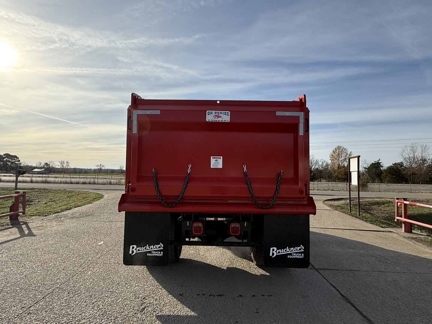 Dump truck bed of a 2025 Mack MD7 dump truck shown from rear view with red body and black mud flaps.