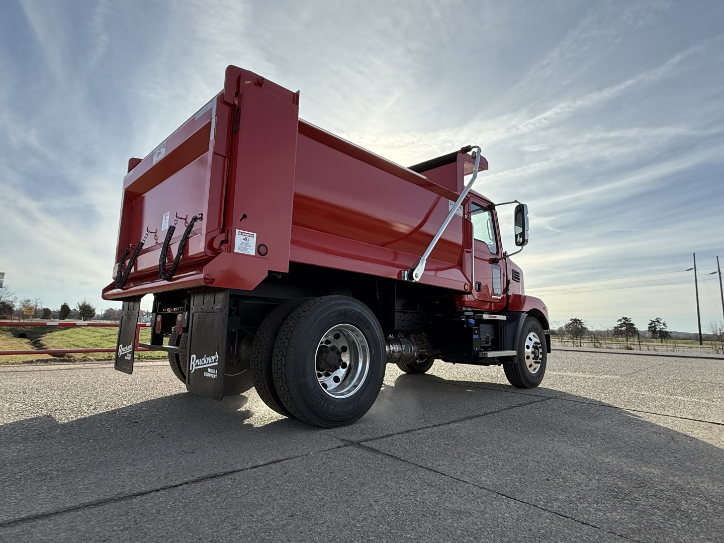 Mack MD7 dump truck in red, rear and passenger side visible, dump bed raised slightly, chrome mirrors, black wheels, side step, VIN badge area not legible.