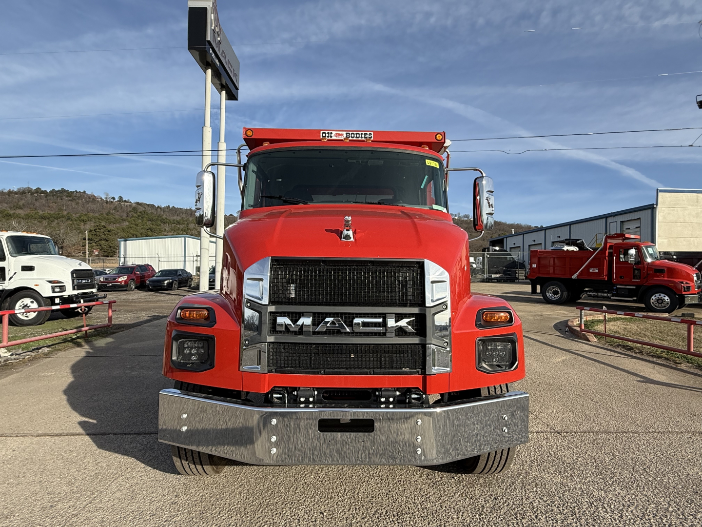 Front view of a red 2025 Mack MD7 dump truck showing bold grille with MACK letters, chrome bumper, headlights, and side mirrors.