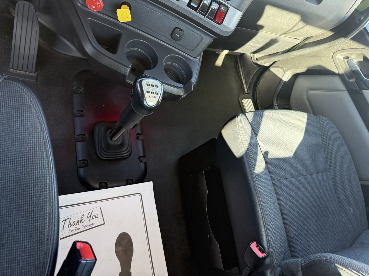 Truck interior with a manual transmission gearshift and center console in a Kenworth T680 cab showing steering wheel and driver seat.