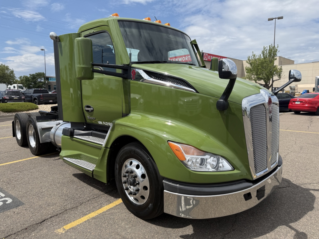 Kenworth T680 cab with lime-green paint showing front grille, headlights, windshield, and side mirror. Visible text includes Kenworth badge on grille, wheel covers, and truck body markings.