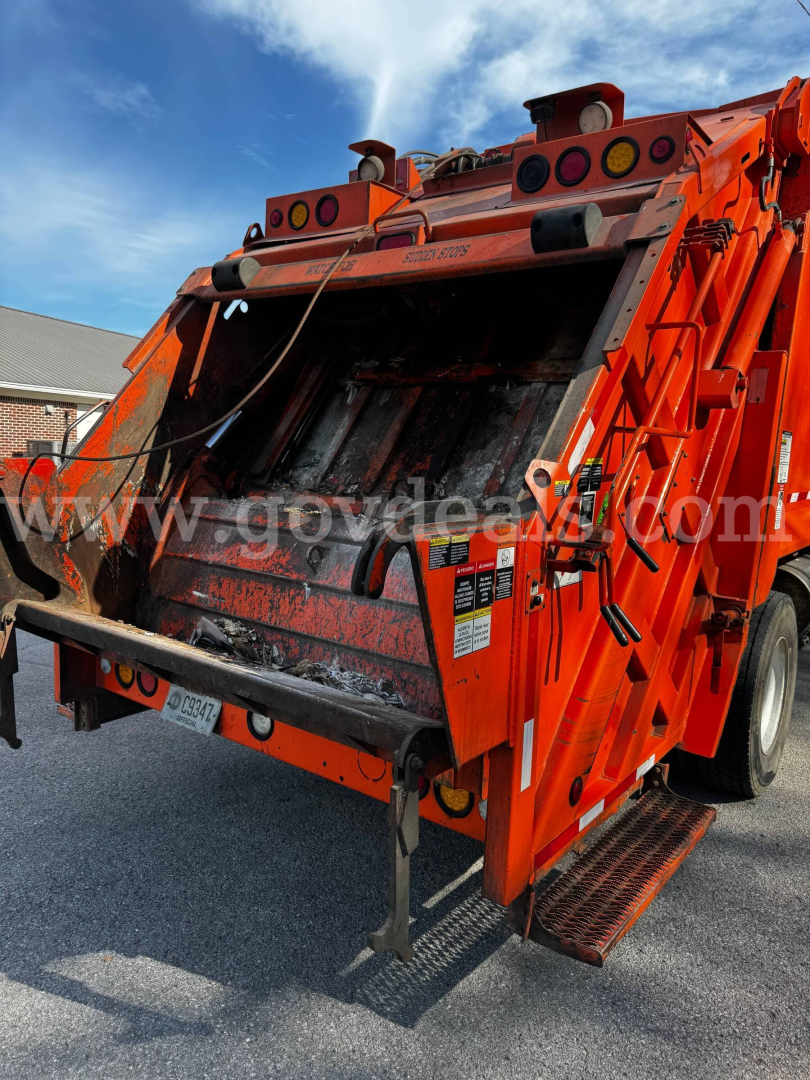Kenworth T370 refuse truck rear hopper open, hydraulic lift gate visible, orange body with warning labels