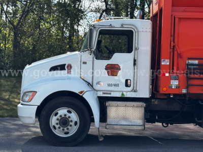Kenworth T370 garbage truck in-service cab side view showing SOLID WASTE badge and reflective decals, white cab, red dump body, fuel cap area, step plate.