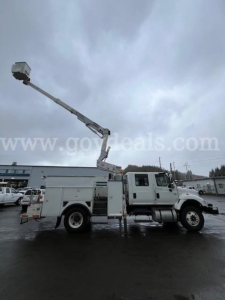 Truck side view of a 2006 International 7400 bucket truck with an extended aerial lift raised, utility body, white cab and chassis, in a parking lot.