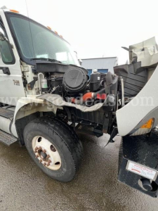 Tractor-trailer truck engine bay showing exposed air filter housing, radiator area, and front wheel with tire; cab and hood open.