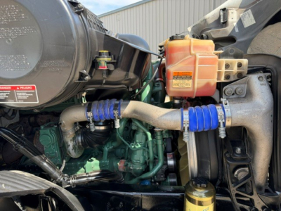 Volvo VNR64T300 engine bay showing coolant reservoir, hoses, and engine components with orange coolant bottle and blue hose clamps.
