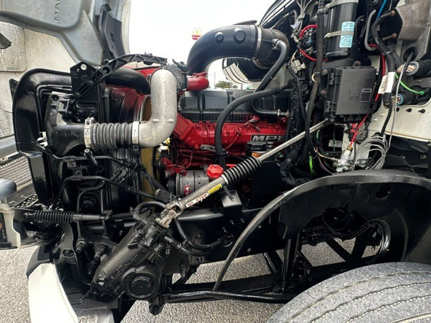 Engine bay of a 2019 Mack Anthem daytime cab truck showing red diesel engine, intake piping, belts, hoses, and surrounding components.