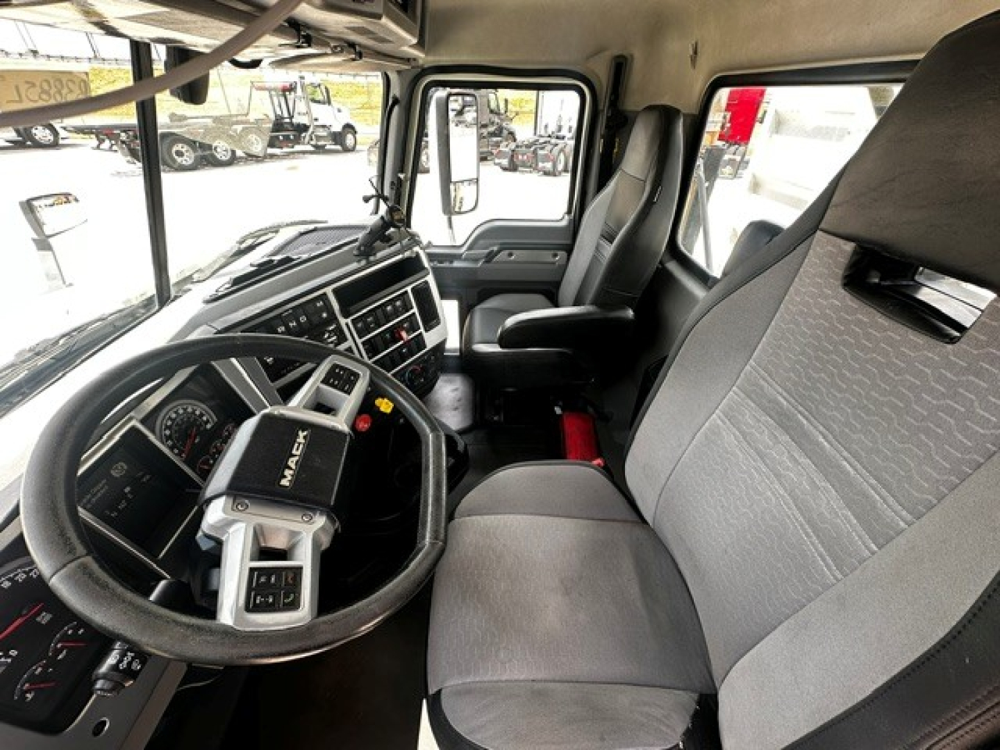 Interior view of a 2019 Mack Anthem truck cab showing steering wheel, dashboard, driver seat, and passenger seat with gray fabric upholstery.
