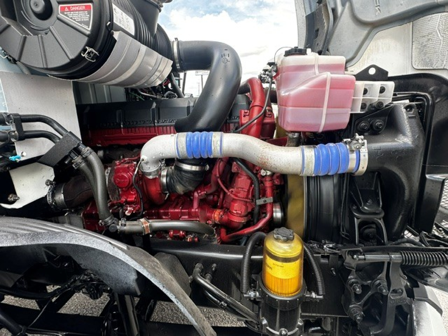 Mack ANTHEM engine bay showing red diesel engine, blue silicone intake hoses, yellow oil filter canister, and pink coolant reservoir.