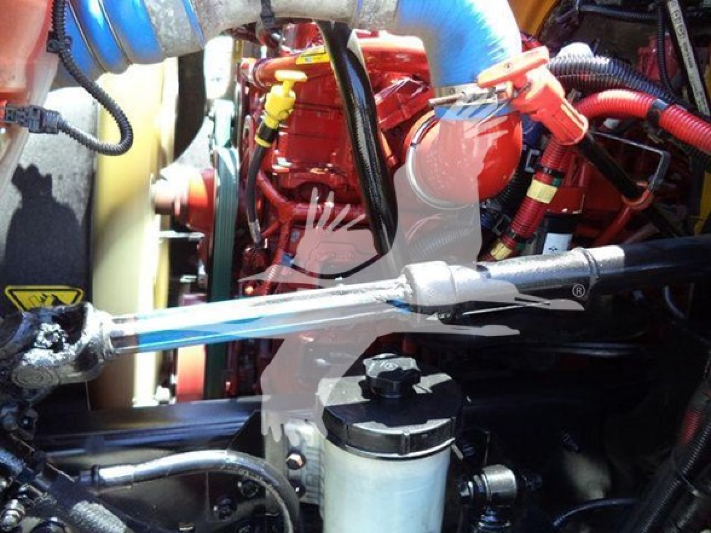 Engine bay of a 2019 International Durastar 4300 with visible hoses, clamps, and a red engine block. Textured components include a black oil fill cap and blue radiator hose.