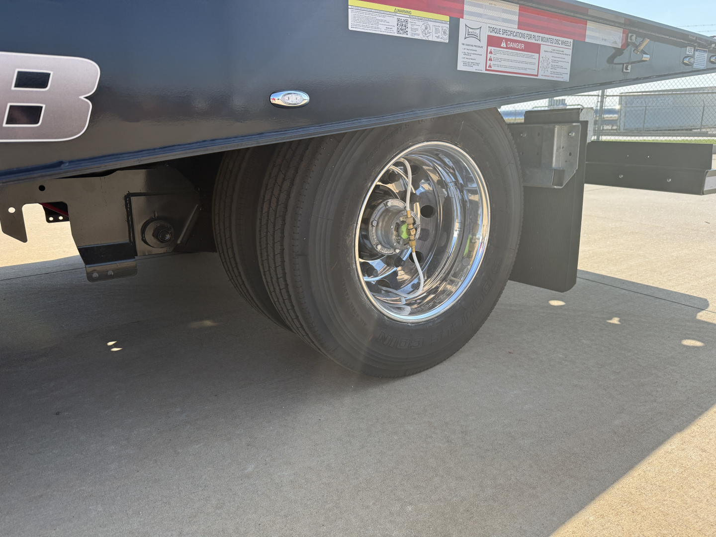 Trailer wheel well and chrome wheel of a 2027 Landoll 455B-53 traveling axle lowboy trailer showing front tire and side decals.