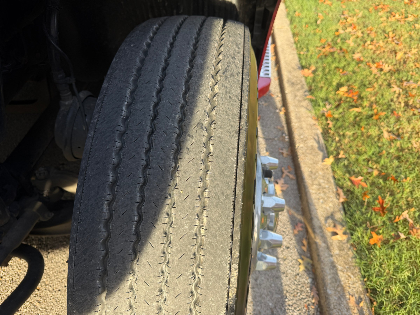 Wheel and tire of a Volvo VNL truck with visible tread and wheel studs; part of the front suspension and wheel assembly.