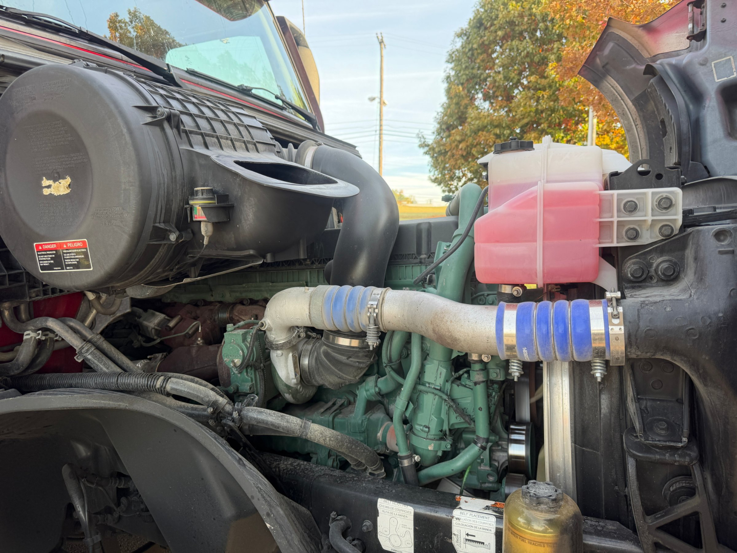 Volvo VNL64T760 engine bay showing air intake, coolant reservoir, blue silicone hoses, green engine block, pink coolant overflow tank and surrounding components.