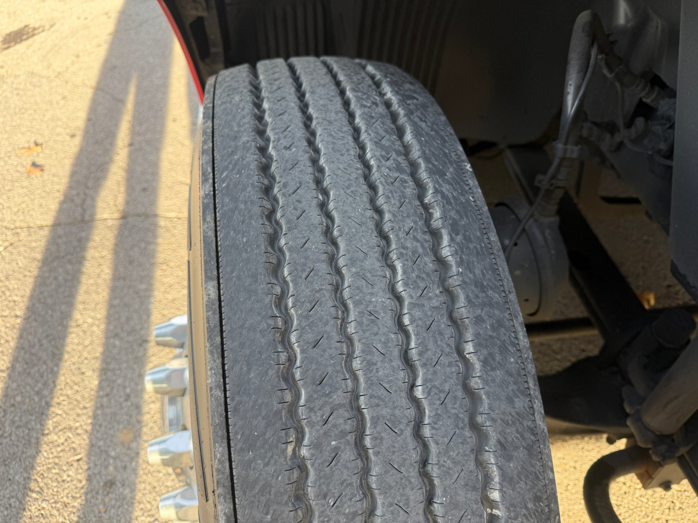 Volvo VNL64T760 truck front wheel and suspension visible; tread worn, steel wheel with lug nuts; part of wheel well and frame visible.