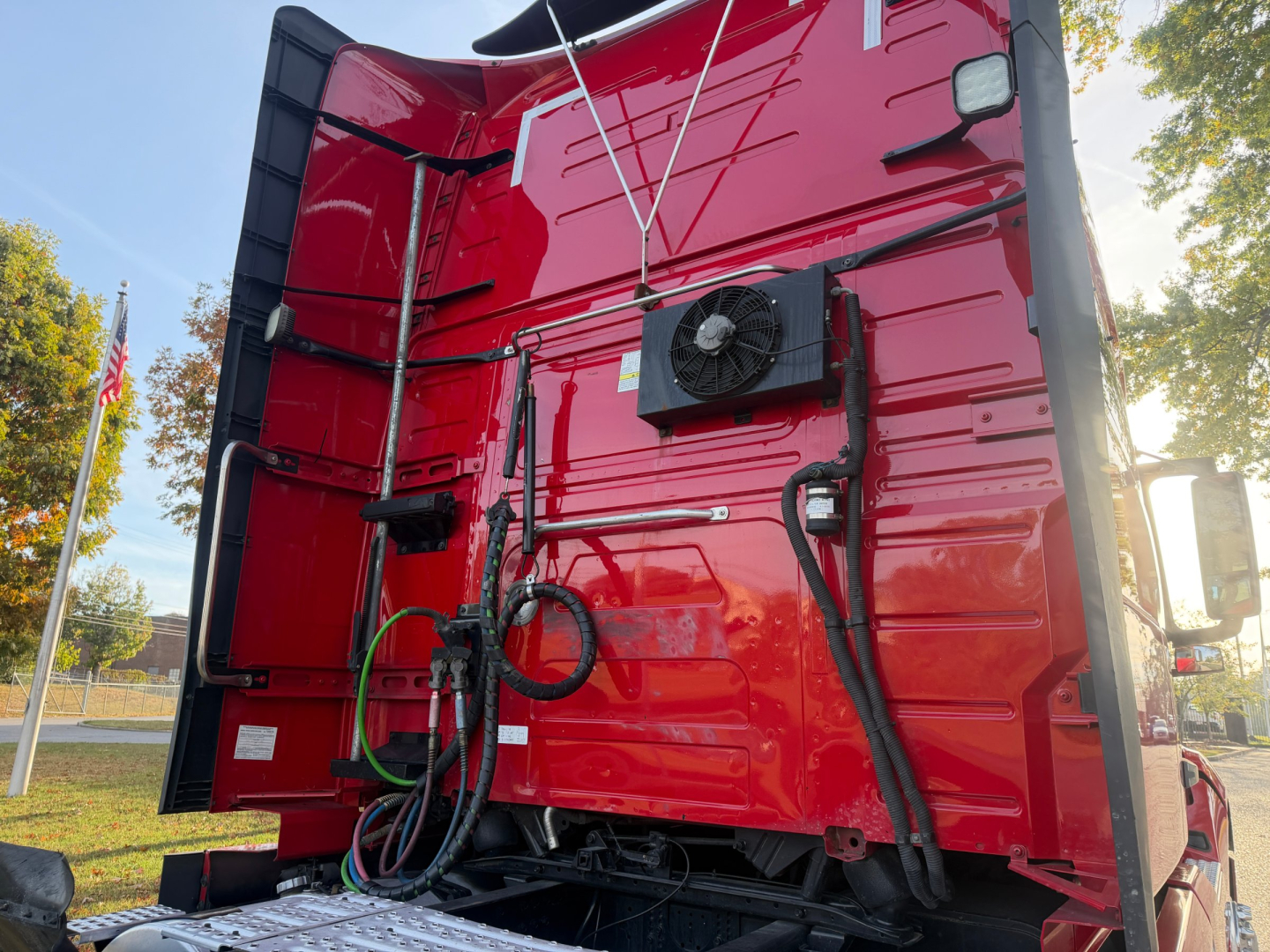 Volvo VNL64T760 rear cab area showing cooling fan and various hoses and wiring harnesses attached to red truck body.