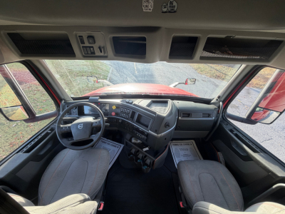 Truck cabin interior of a Volvo VNL series showing the dashboard and steering wheel, with two seats and overhead controls.