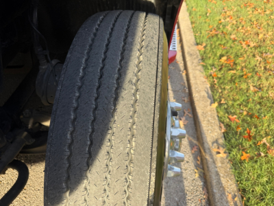 Wheel and tire of a Volvo VNL truck with visible tread and wheel studs; part of the front suspension and wheel assembly.