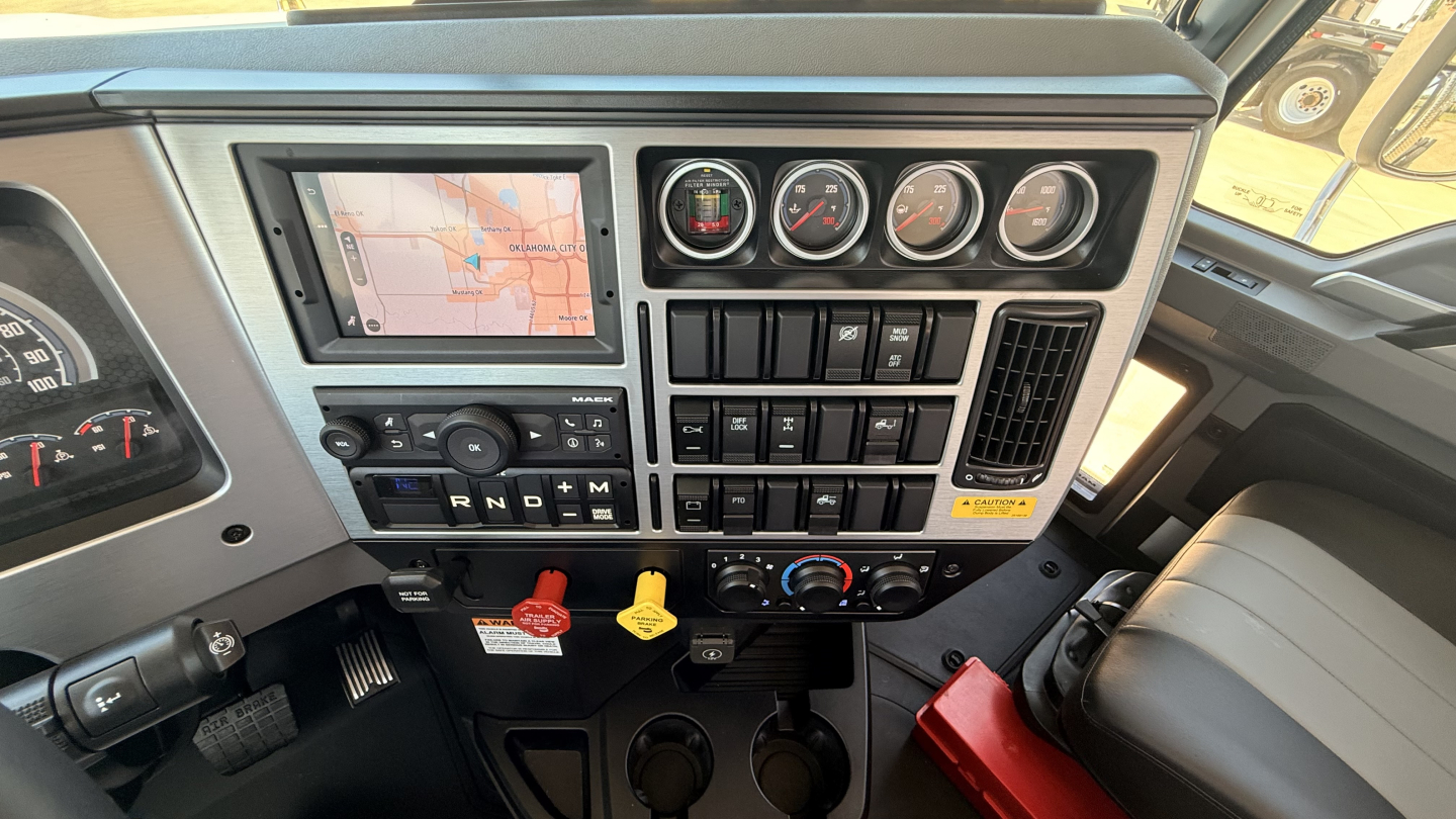 Mack PI64T cab dashboard showing GPS display, analog gauges, climate controls, and ignition area.