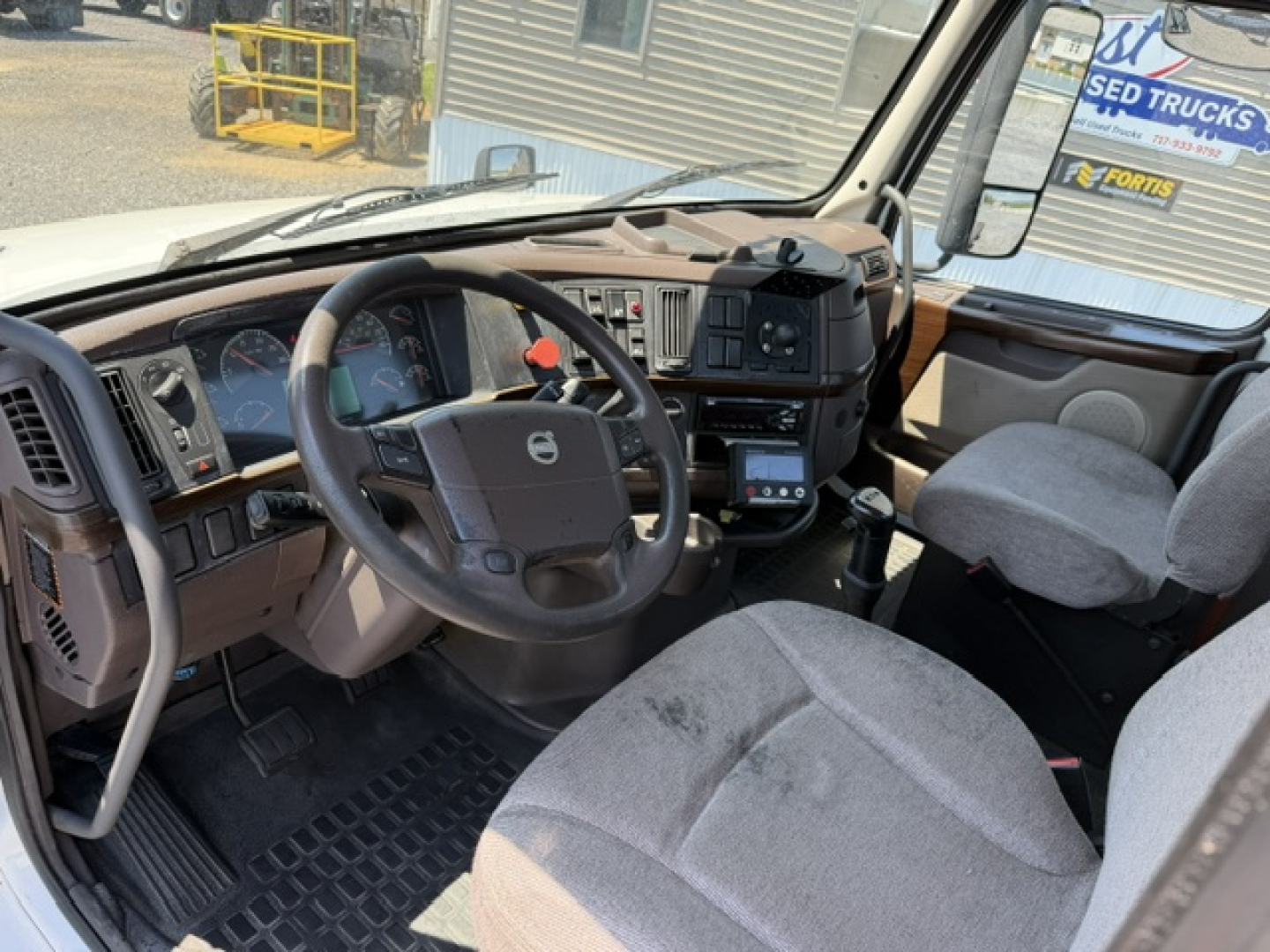 Volvo truck cab interior showing steering wheel, dashboard, and front seats in a day cab truck.