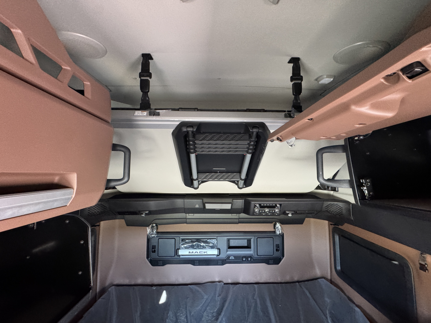 Interior of a new Mack PR64T76H truck cab showing overhead bunk area and control panel with 'MACK' logo on a dash panel.