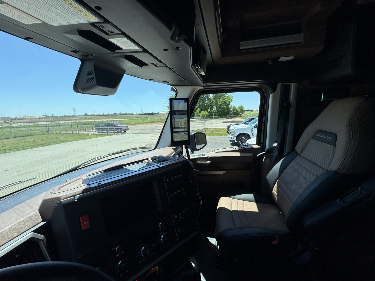 Truck cab interior showing dashboard with steering wheel, large side window, and captain seat; door window; overhead console and mirrors visible.