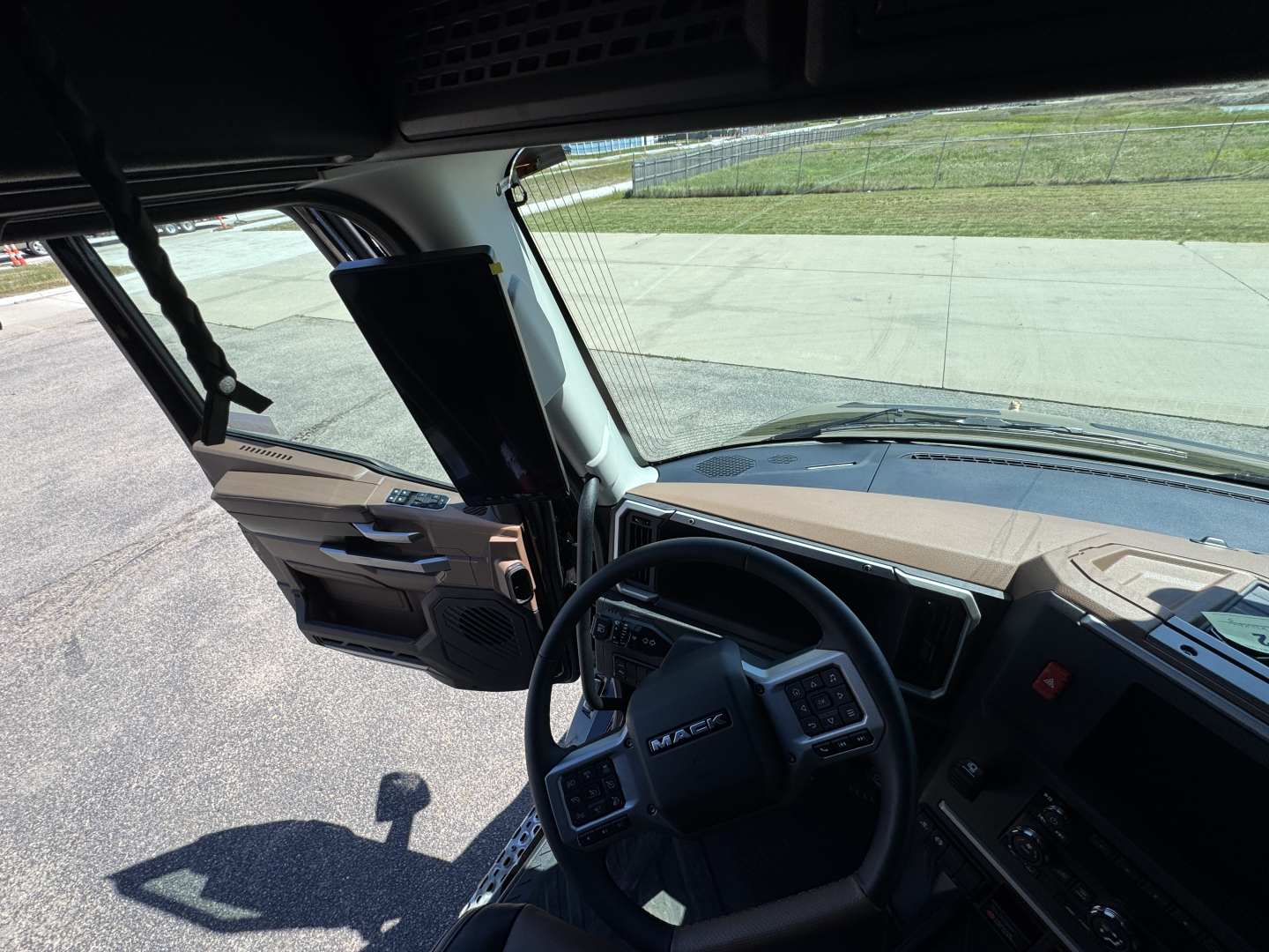 Mack PR64T76H conventional sleeper truck interior view from driver seat showing steering wheel, dashboard, and door panels.