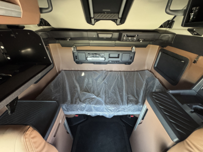 Cab interior of a Mack truck with brown and black panels, bed area covered in protective plastic, center console, and storage compartments visible.