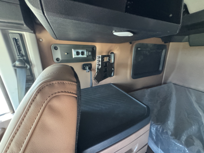 Cab interior of a new Mack PR64T76H truck showing a control panel, power outlet, and seating area in beige/brown colors.