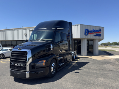 Black Mack tractor with aerodynamic cab in front of a dealership building labeled Brandenburg’s selling Mack PR64T76H truck new in stock.