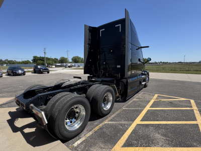 Mack PR64T76H conventional sleeper truck rear-left view showing tandem axles and sixth wheel area with clean glossy black cab.