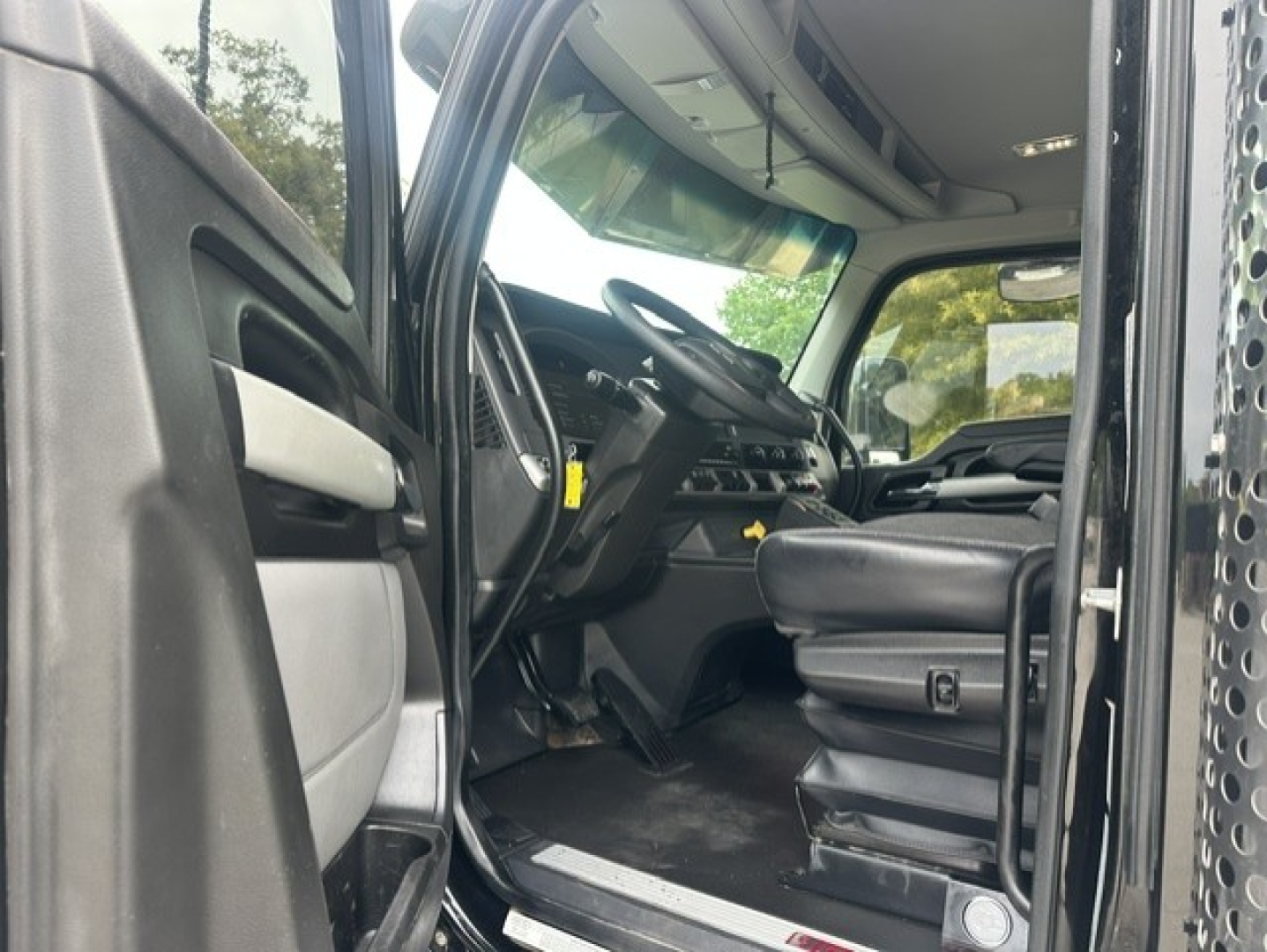 Kenworth T880 truck cab interior with driver seat, dashboard, and open door; steering wheel and controls visible.