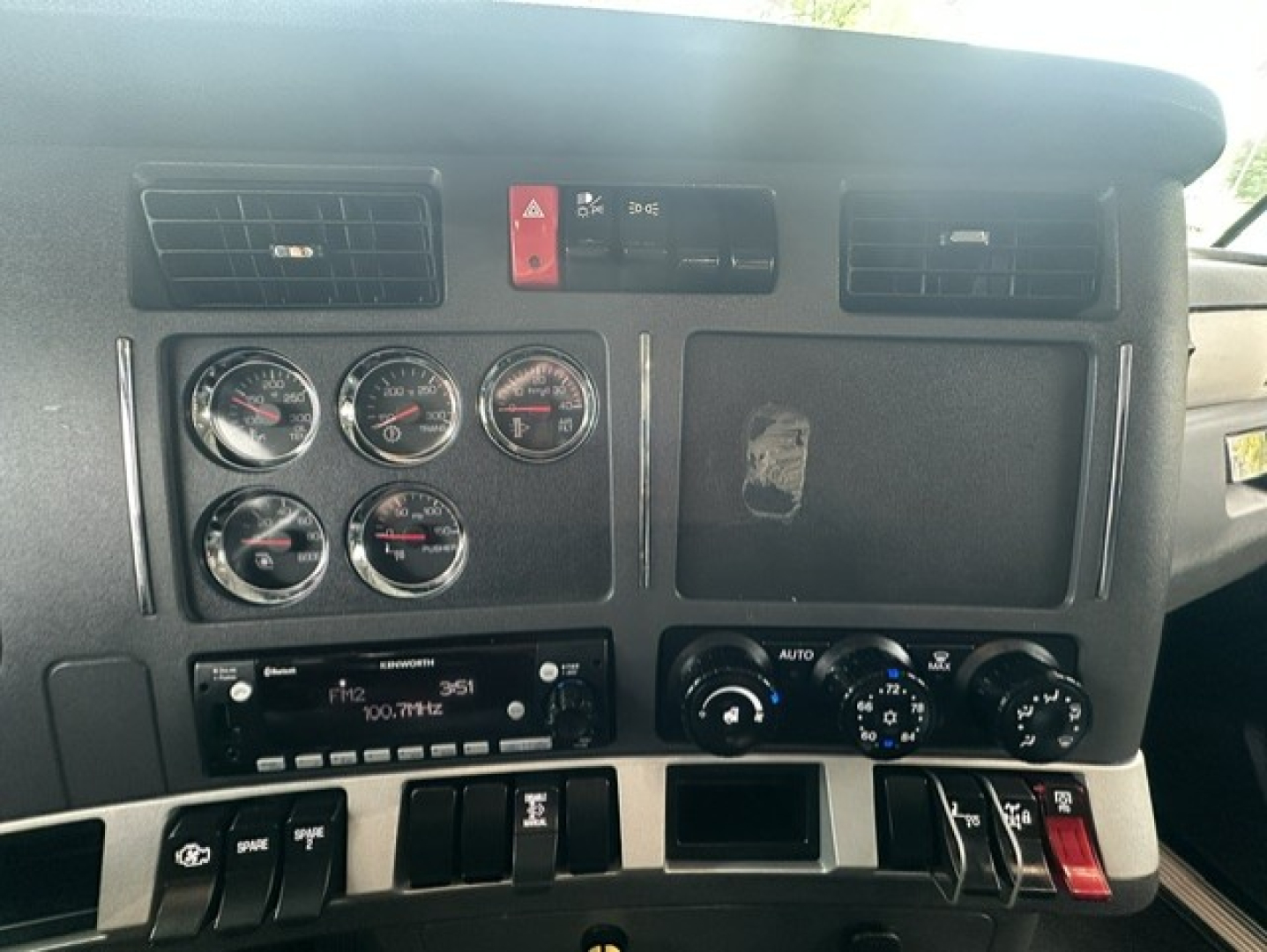 Dashboard panel of a Kenworth T880 showing multiple round gauges, switches, vents, and an Auto climate control knob.