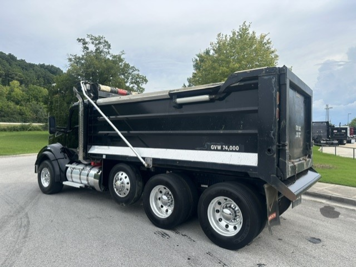Kenworth T880 dump truck with black dump box and white reflective stripe, three rear axles, side view.