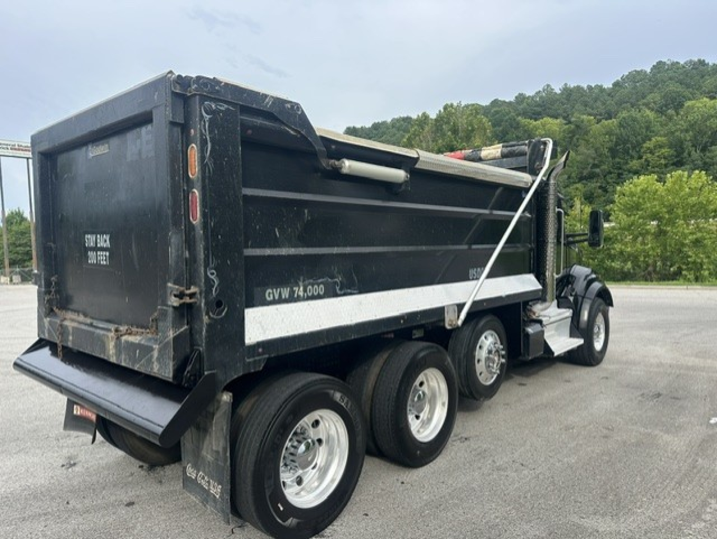 Kenworth T880 dump truck side rear showing GVW 74,000 and dump bed with black paint, white stripe, and triple rear axles.