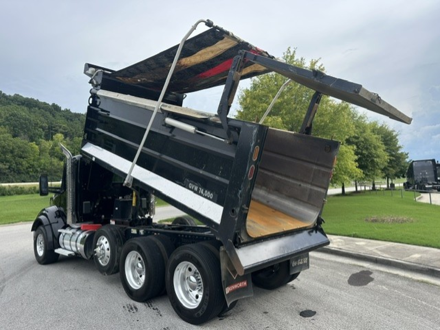 Kenworth T880 dump truck in-service showing open dump bed with hydraulic mechanism and triple rear axles.